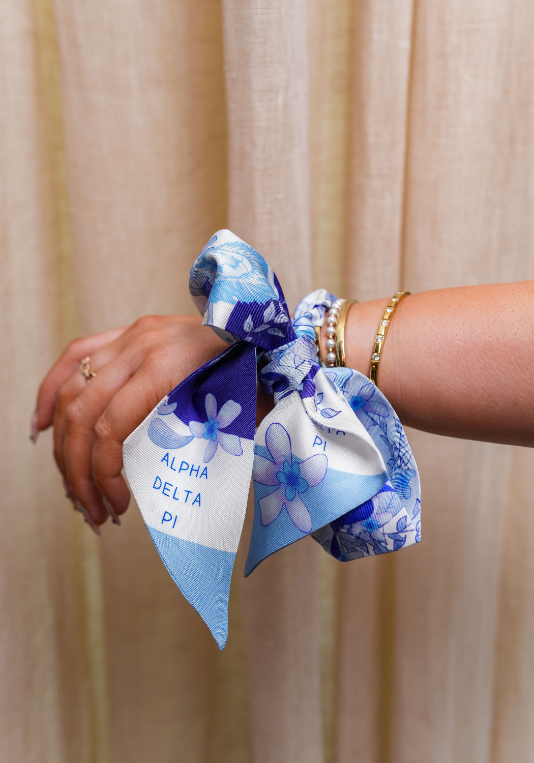 Blue and white floral scarflette with Alpha Delta Pi lettering tied on wrist with gold bracelets.