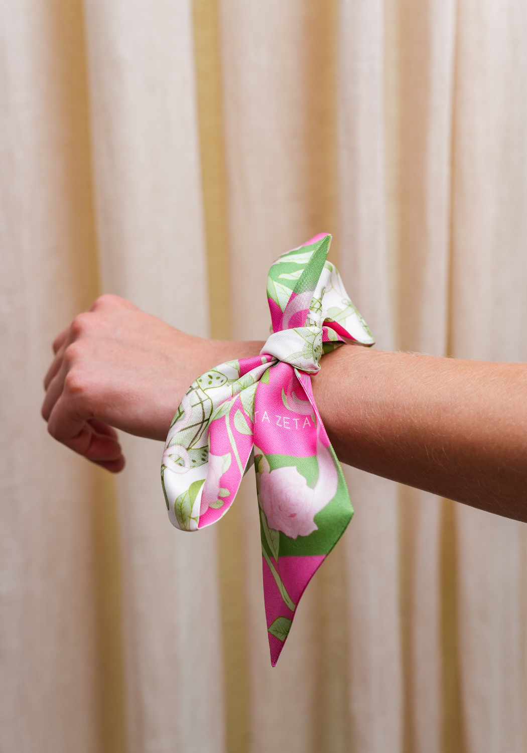 Pink and green floral silk scarf tied around wrist as a bracelet accessory.