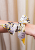 Yellow and gray floral silk scarf tied around wrist with Kappa Alpha Theta tag.