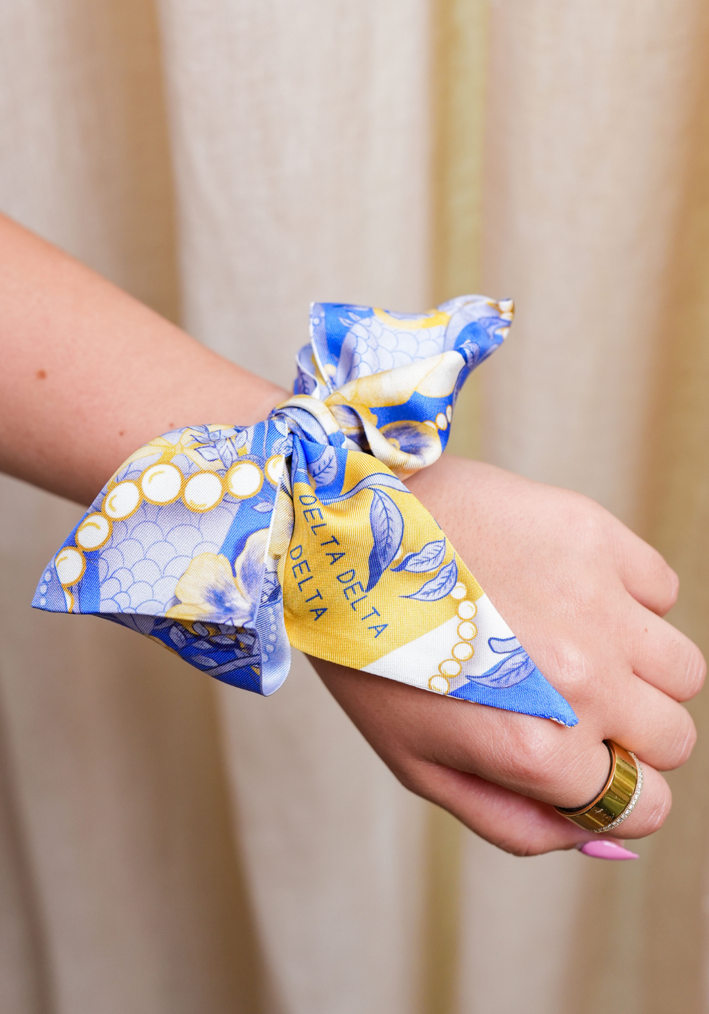 Blue and yellow patterned silk scarflette tied around wrist with Delta Delta Delta lettering.
