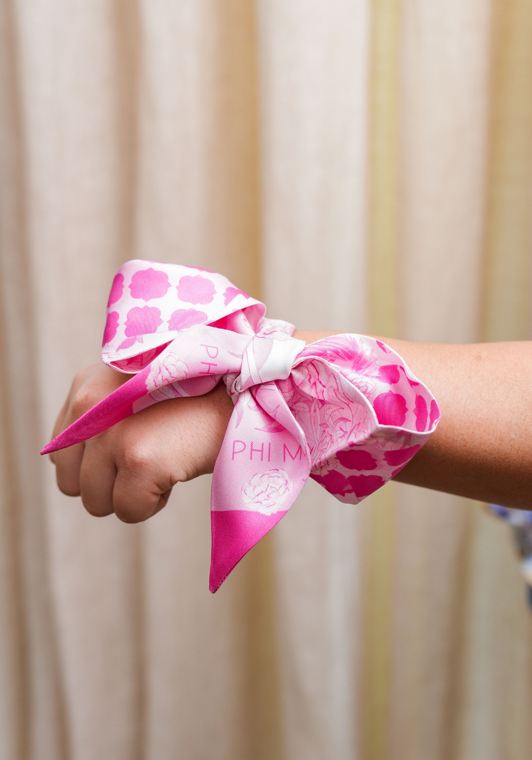 Pink and white Phi Mu scarflette tied around wrist with floral and geometric patterns.