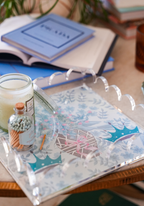 Clear acrylic tray with scalloped edges and blue crown motifs on a floral background.