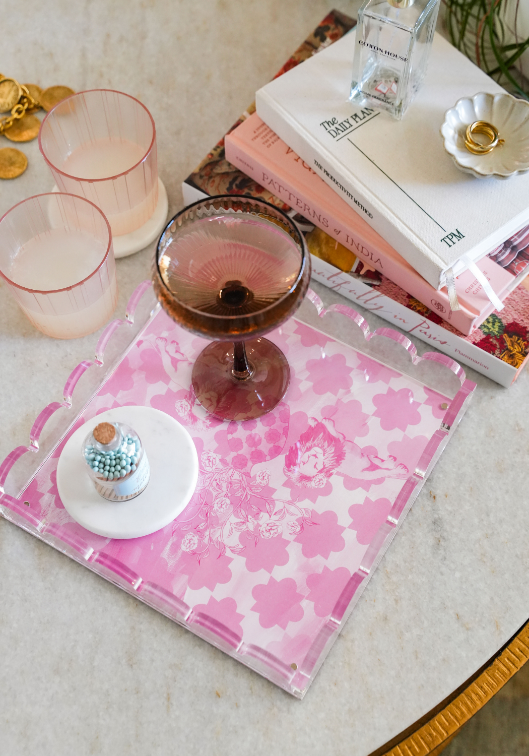 Pink scalloped tray with floral pattern holding two pink-rimmed glasses, a purple coupe glass, and a small white plate with.