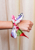 Silk scarflette with purple and green floral patterns and red trim tied around wrist with pearl bracelet.