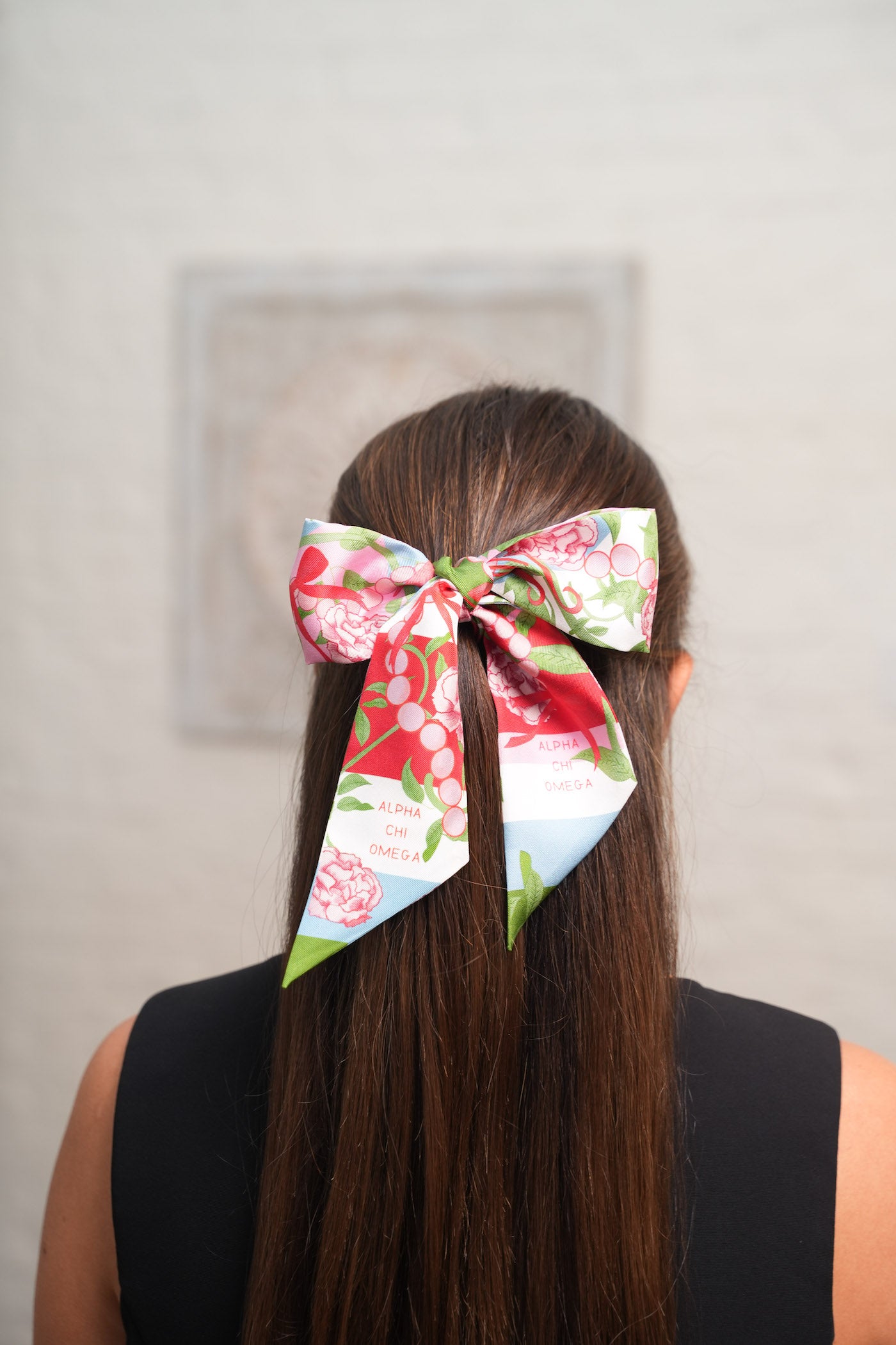 White scarflette with pink and red floral print tied in a bow on long brown hair.