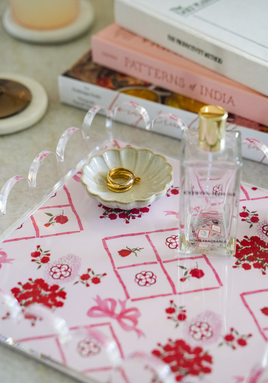 Clear acrylic tray with scalloped edges on pink and red floral fabric, holding a gold shell dish and clear perfume bottle.