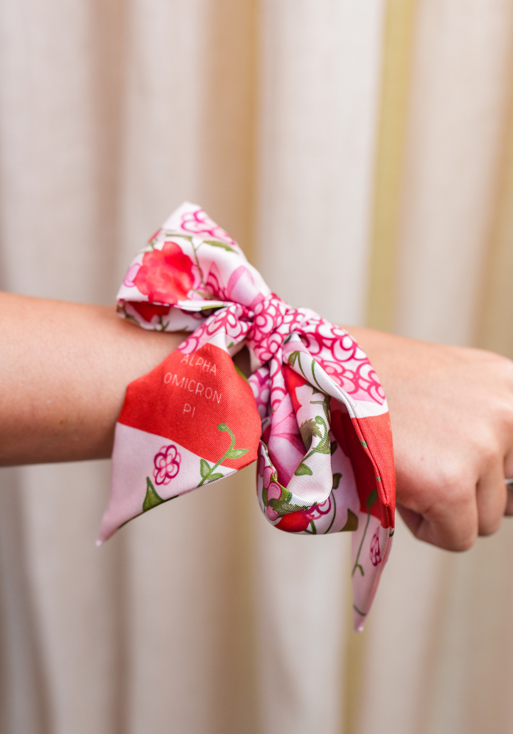 Silk scarflette with pink, red, and white floral patterns tied around wrist.