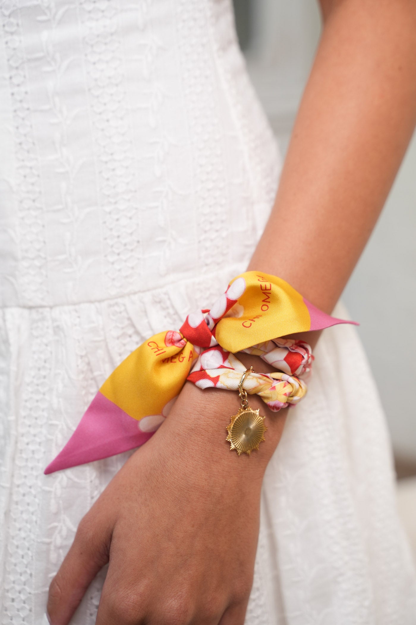 Silk scarflette with yellow, pink, and cream floral patterns tied on wrist with gold charm bracelet.