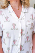 White pajama top with pink floral print, short sleeves, collar, and front pocket with purple trim.