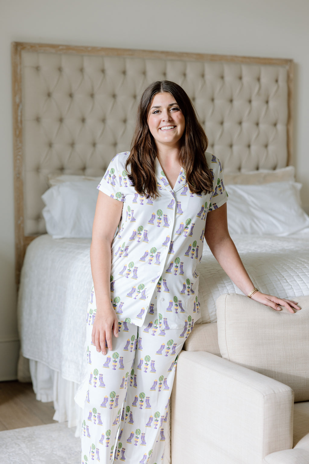 White short-sleeve pajama set with purple and green Mardi Gras bead print on woman in bedroom.