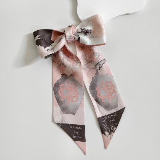 Pink and gray silk scarflette with Gamma Phi Beta logos and floral accents, tied in a bow.