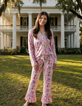 Woman wearing a floral pajama set in front of a large house.